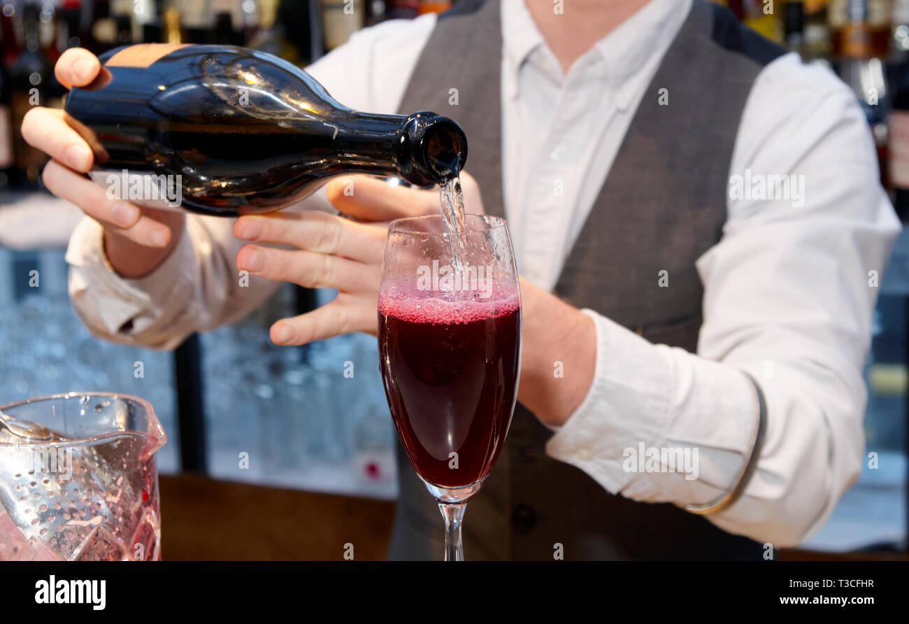 Il barista è versando il vino spumante nella produzione di vetro arbusto cocktail Foto Stock