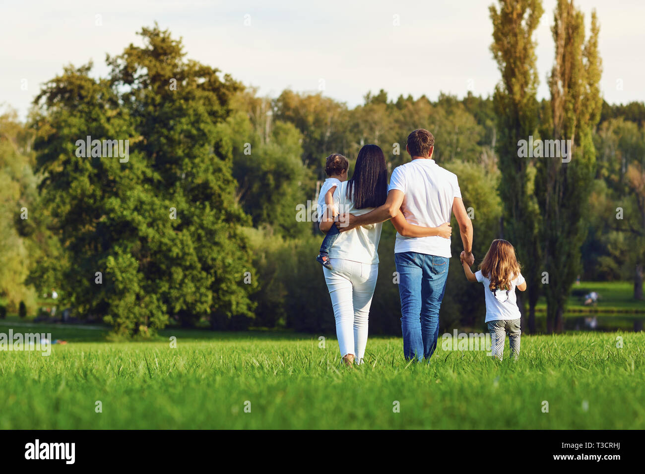 Vista posteriore. La famiglia felice con bambini passeggiate nel parco. Foto Stock