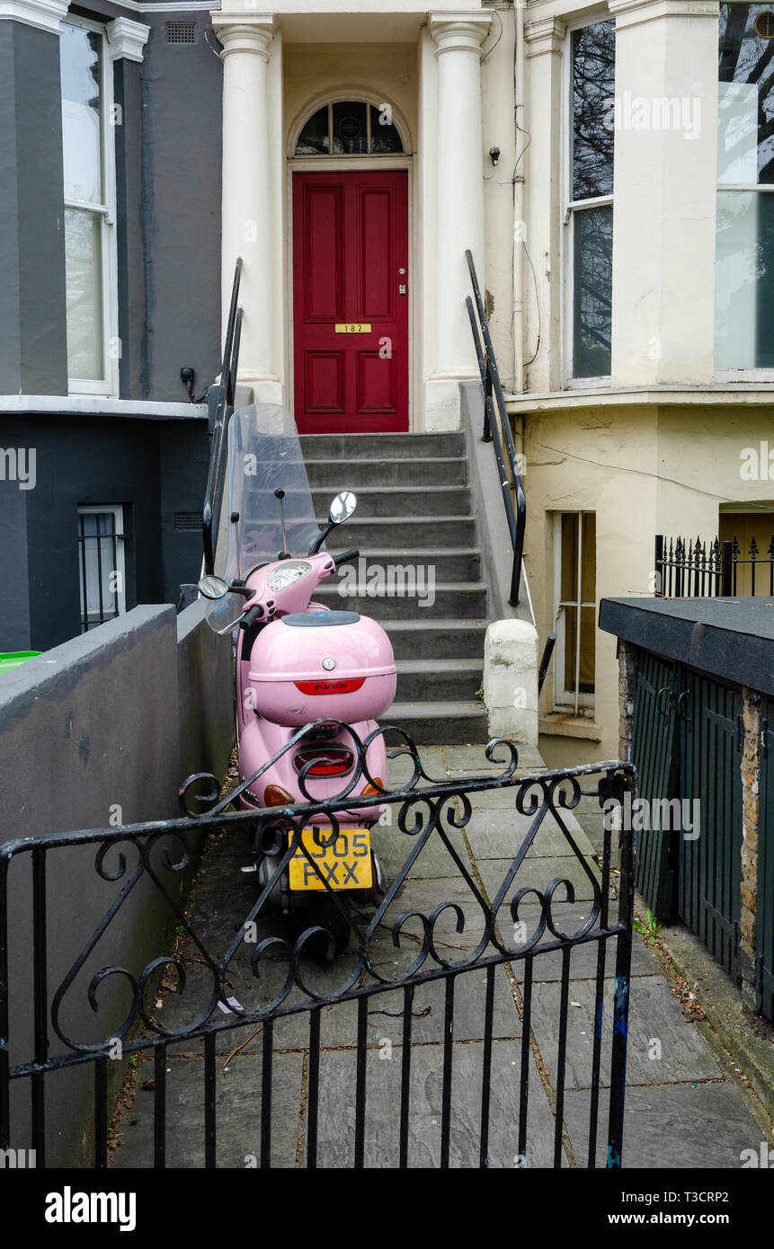 Una rosa scooter è parcheggiato su un percorso di giardino nella parte anteriore dei gradini che portano fino a una porta anteriore in una casa a Londra/ Foto Stock