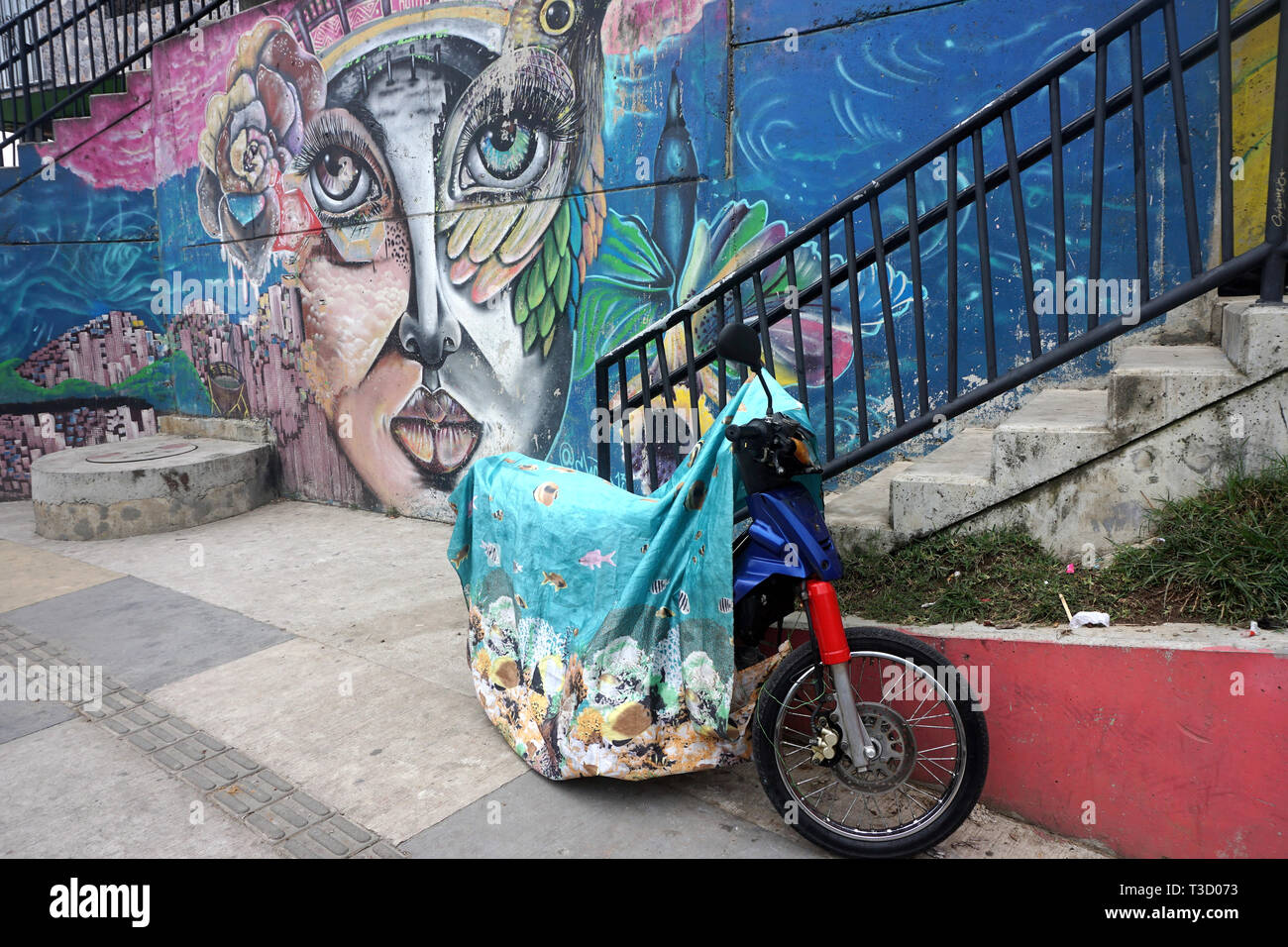 Motocicletta sotto il coperchio colorato nella parte anteriore del vivace murale nel Comuna 13, Medellin, Colombia Foto Stock