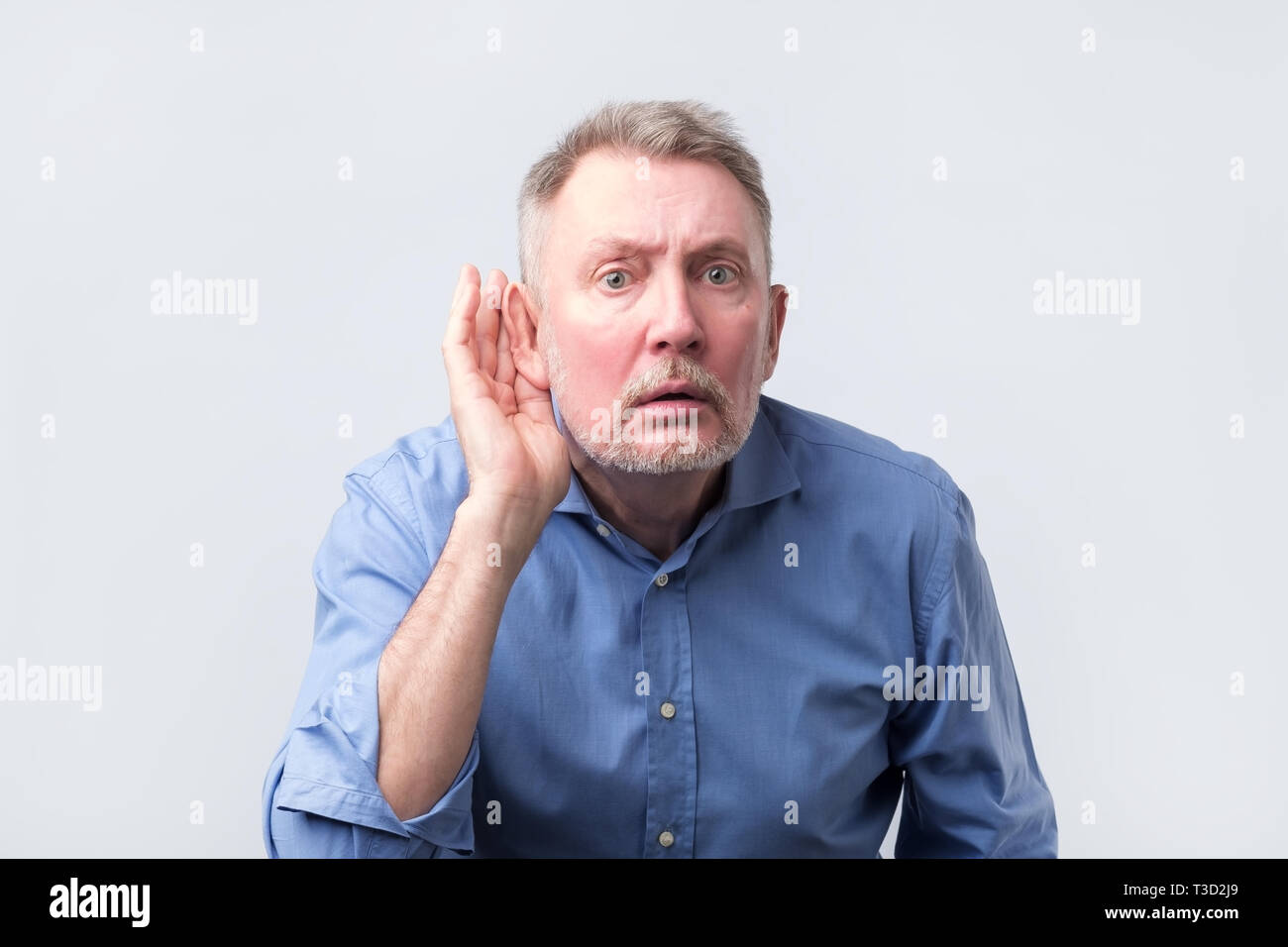 Senior Uomo in camicia blu che soffre di sordità. Egli vuole sentire voci fresche. Foto Stock