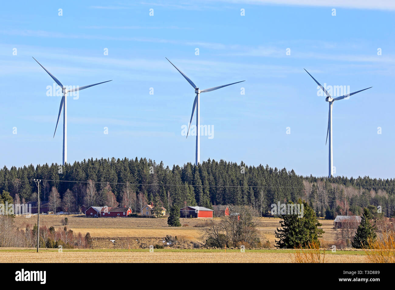 Fila di tre turbine eoliche paese vicino villaggio nel sud della Finlandia in una giornata di sole di primavera. Foto Stock