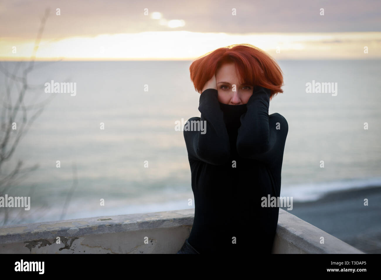 Ritratto di una giovane donna con i capelli rossi e piercing guardare sullo sfondo del mare e del tramonto Foto Stock