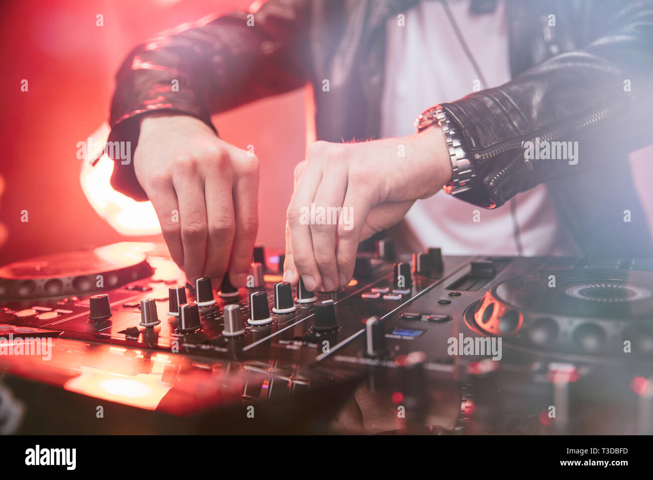 Il mixaggio DJ al party festival con la luce rossa e il fumo in background - Estate vista notturna della discoteca all'interno. Focus sulle mani Foto Stock