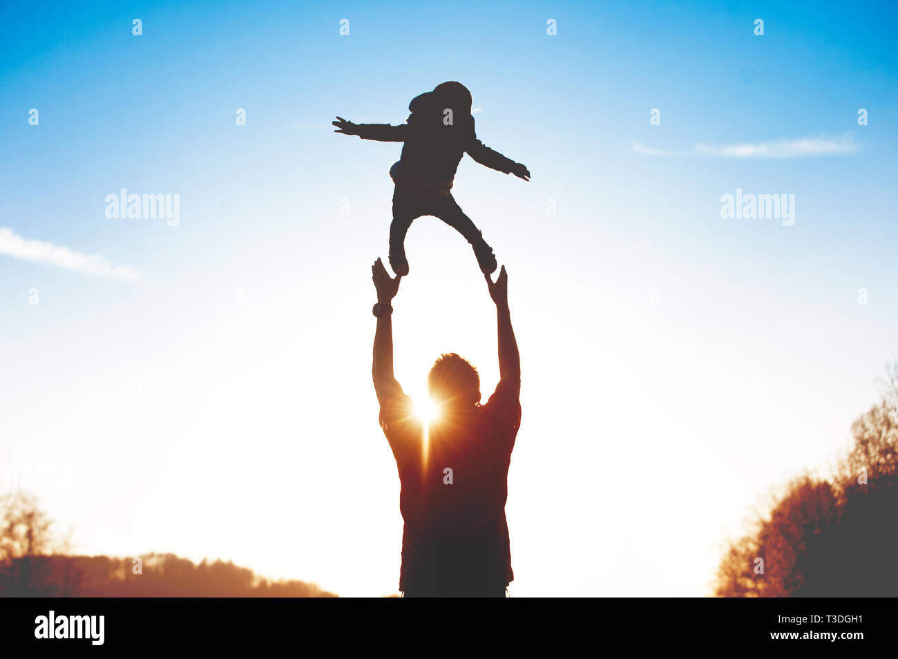 Padre Throwns bambino nell'aria. Silhouette non riconoscibile nel tramonto. Foto Stock