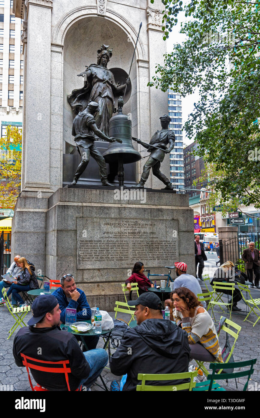 Herald Square, New York City, nello Stato di New York, Stati Uniti d'America. Persone in relax outdoor cafe tabelle . Alle loro spalle il memoriale a James Gordon Bennett, 1795- Foto Stock