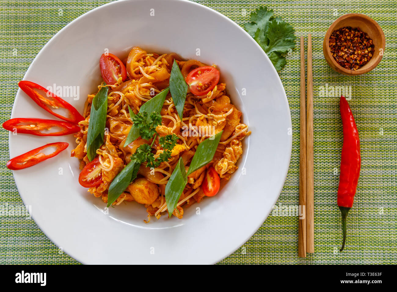 Tailandese tradizionale piatto a base di noodle Pad Thai servita sul piatto di portata in ceramica bianca. Bacchette di legno e peperoncino secco sul lato. Vista dall'alto. Foto Stock