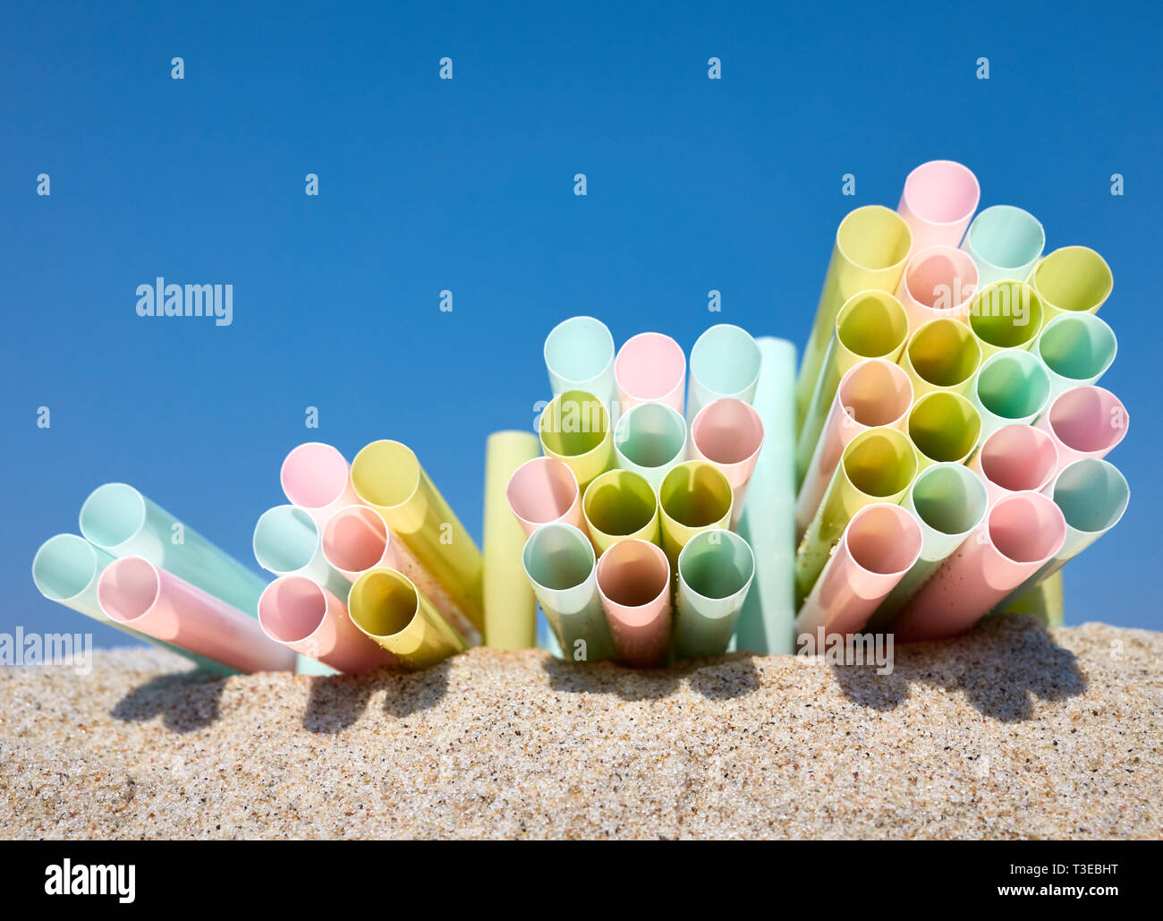 Pile di coloratissimi cannucce di plastica sulla sabbia contro il cielo blu, il fuoco selettivo. Foto Stock