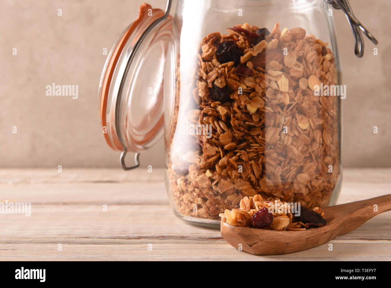 Primo piano della memorizzazione di un vaso riempito con muesli fatti in casa con il coperchio aperto e un cucchiaio in primo piano. Formato orizzontale con copia spazio. Foto Stock