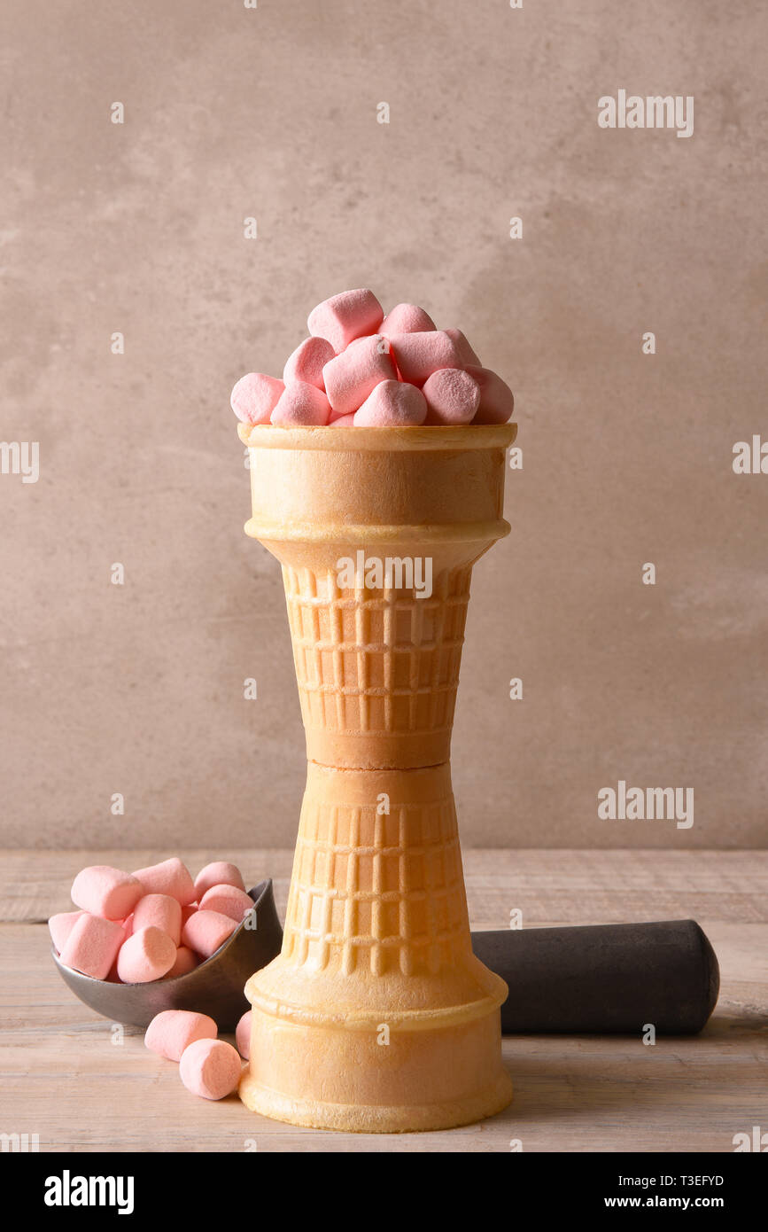 Impilati coni gelato riempito con il colore rosa marshmallows e uno scoop in background. Foto Stock