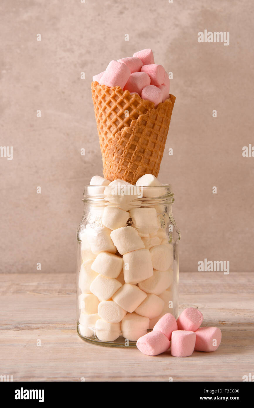 Lo zucchero a cono gelato in piedi in un barattolo di mini marshmallows e riempito con il colore rosa marshmallows. Foto Stock