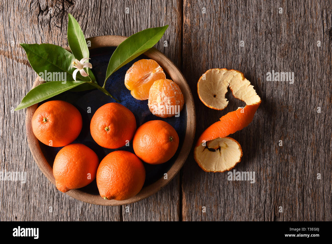 I Tangelos Minneola: primo piano della frutta sbucciata su una piastra con foglie e fiori d'arancio su una tavola in legno rustico. Foto Stock