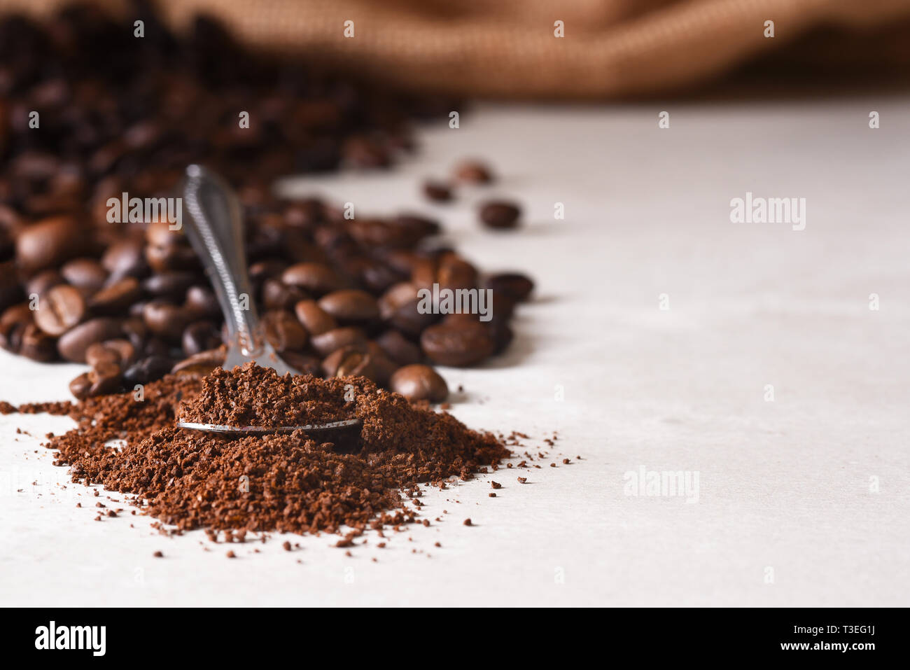 Primo piano di un cucchiaio di caffè macinato con fagioli whoel fuoriuscita di un sacco di tela in background. Profondità di campo. Foto Stock