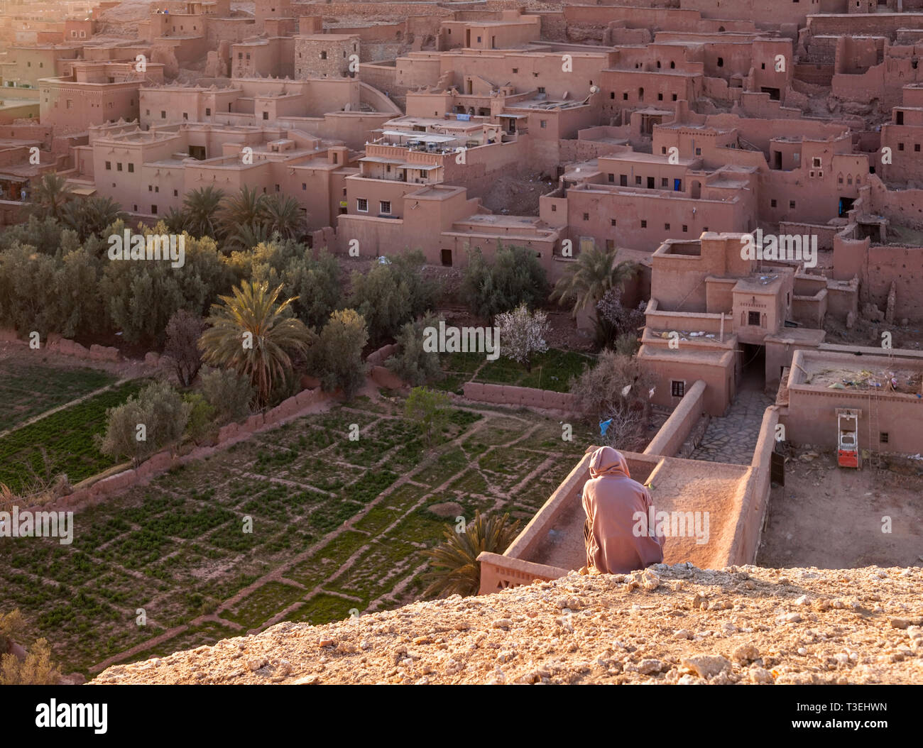 Un uomo seduto su di una collina che guarda verso il Ksar Aït-Ben-Haddou, Aït Benhaddou‌, provincia di Ouarzazate, Drâa-Tafilalet, Marocco, Africa. Foto Stock