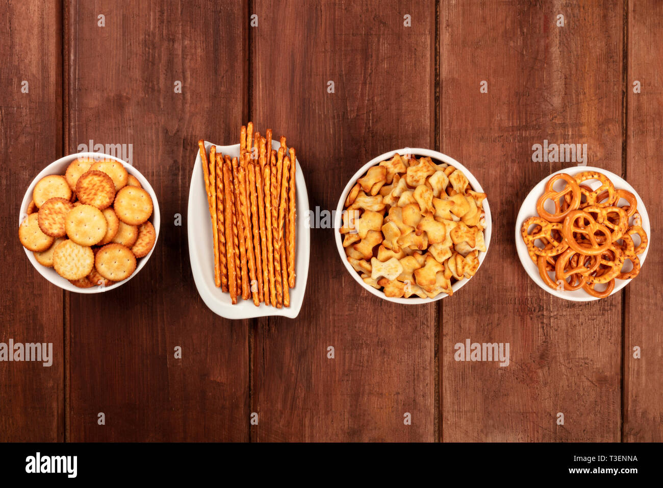Il salato crackers, bastoncini, salatini e goldfishes, girato dalla parte superiore su di un legno scuro dello sfondo con copia spazio. Party Mix snack Foto Stock