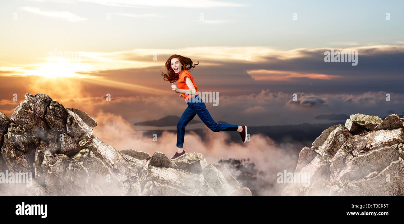 Redhead donna salta alla scogliera sul cielo blu sullo sfondo. Foto Stock