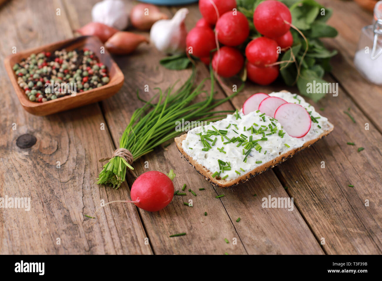 Una sana prima colazione - fette biscottate con quark e di erba cipollina fresca, ravanelli e pomodori su una tavola in legno rustico - una sana colazione con erbe fresche Foto Stock