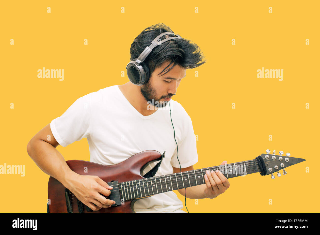 Bel giovane uomini asiatici a suonare la chitarra e ascoltare musica con le cuffie isolato su sfondo giallo Foto Stock