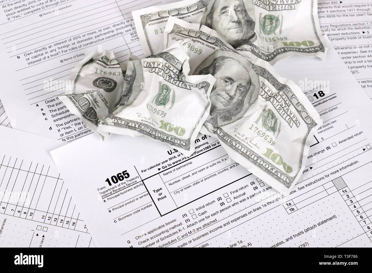 1065 forma fiscale si trova nei pressi di accartocciata Hundred Dollar Bills su un tavolo. Noi tornare per reddito parentship Foto Stock