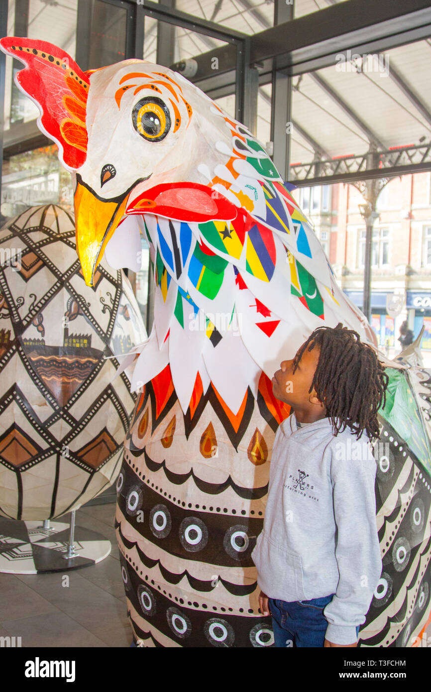 Gigantesco pollo di carta pasquale oversize in esposizione nel centro della città. TADIWA CHAPARADZA (MR) 10 anni è incuriosito dalla grande scultura di scarafaggio Papier-Mache. Le figure degli animali natalizi di Pasqua in mostra, alte due metri, le attrazioni sono collocate fuori dal mercato di Preston. Keith Ogden, un artista locale, è l'uomo dietro l'attrazione dipinta a mano. Le uova sono a tema intorno al patrimonio industriale della città e paesaggi Lancashire. I mercati di Preston espongono le uova di Pasqua giganti per la competizione di selfie durante le vacanze di Pasqua. Foto Stock