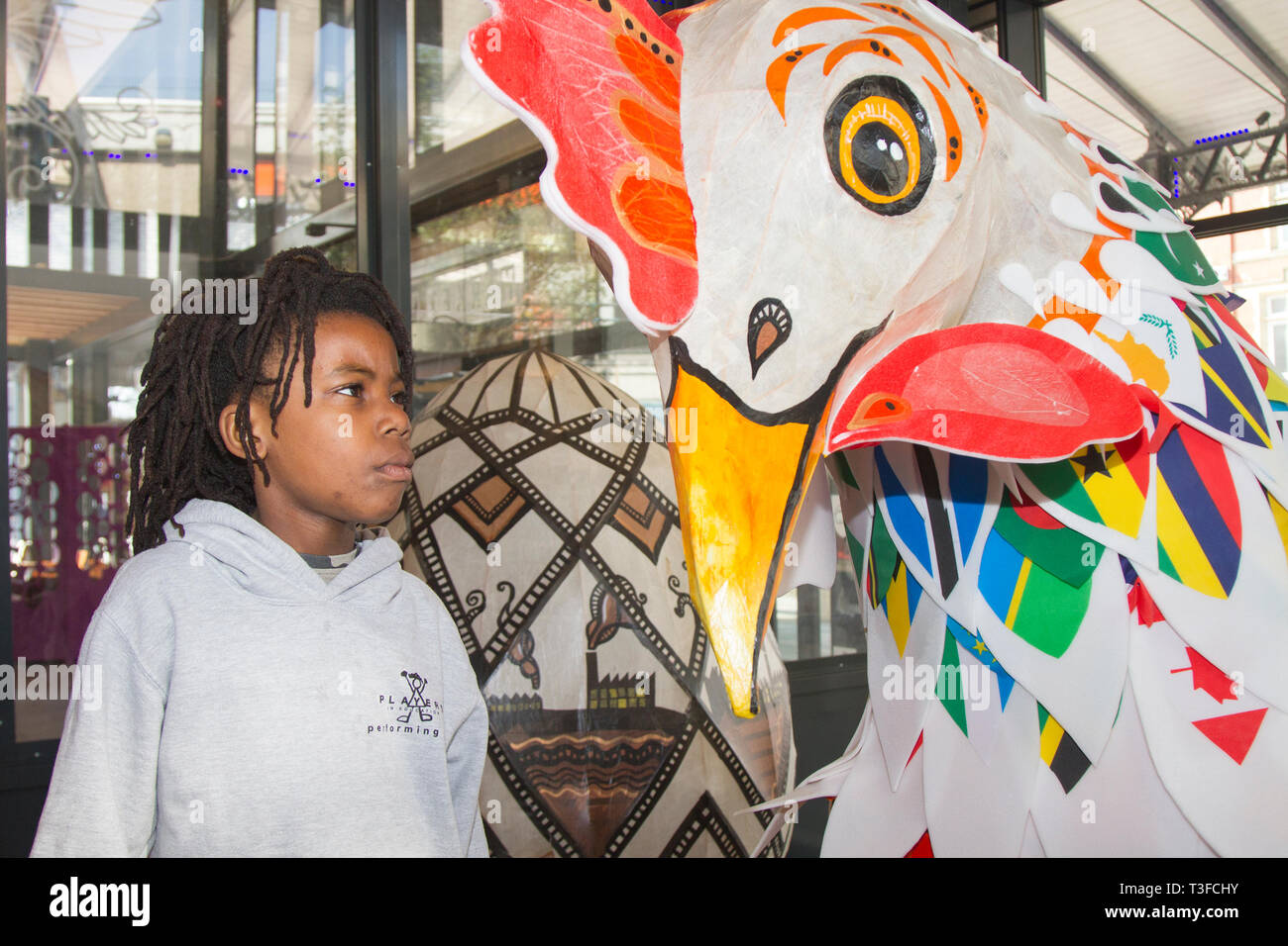 Gigantesco pollo di carta pasquale oversize in esposizione nel centro della città. TADIWA CHAPARADZA (MR) 10 anni è incuriosito dalla grande scultura di scarafaggio Papier-Mache. Le figure degli animali natalizi di Pasqua in mostra, alte due metri, le attrazioni sono collocate fuori dal mercato di Preston. Keith Ogden, un artista locale, è l'uomo dietro l'attrazione dipinta a mano. Le uova sono a tema intorno al patrimonio industriale della città e paesaggi Lancashire. I mercati di Preston espongono le uova di Pasqua giganti per la competizione di selfie durante le vacanze di Pasqua. Foto Stock