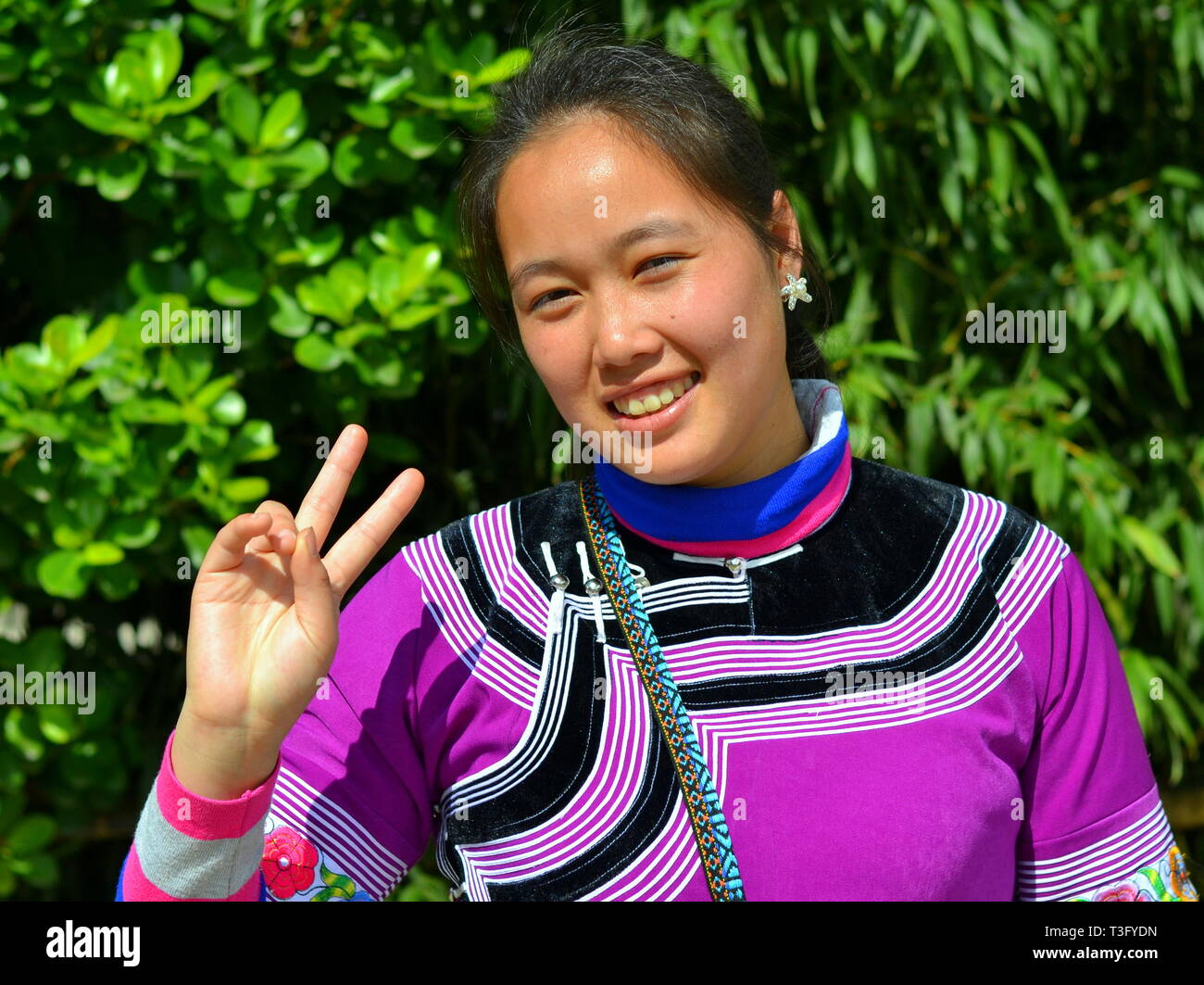 Giovani cinesi Miao donna (appartenenti a una minoranza etnica) indossa un colorato tradizionale abito etnici e lampeggia il V segno. Foto Stock