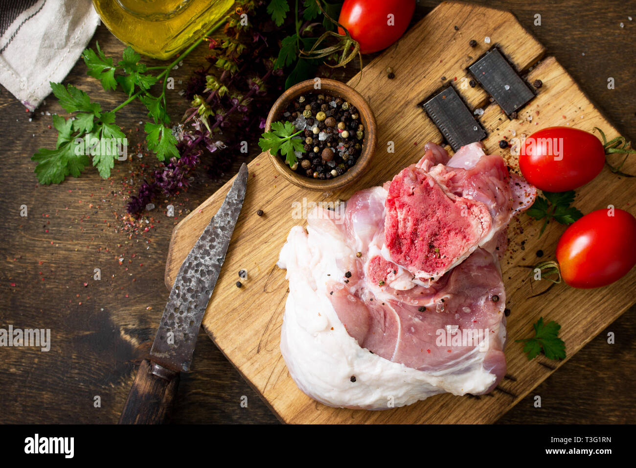 Fresco la carne cruda. Carne di maiale cruda bistecca con l'olio d'oliva, i pomodori e le erbe sul tavolo di legno. Vista superiore piatta sfondo laici con copia spazio. Foto Stock