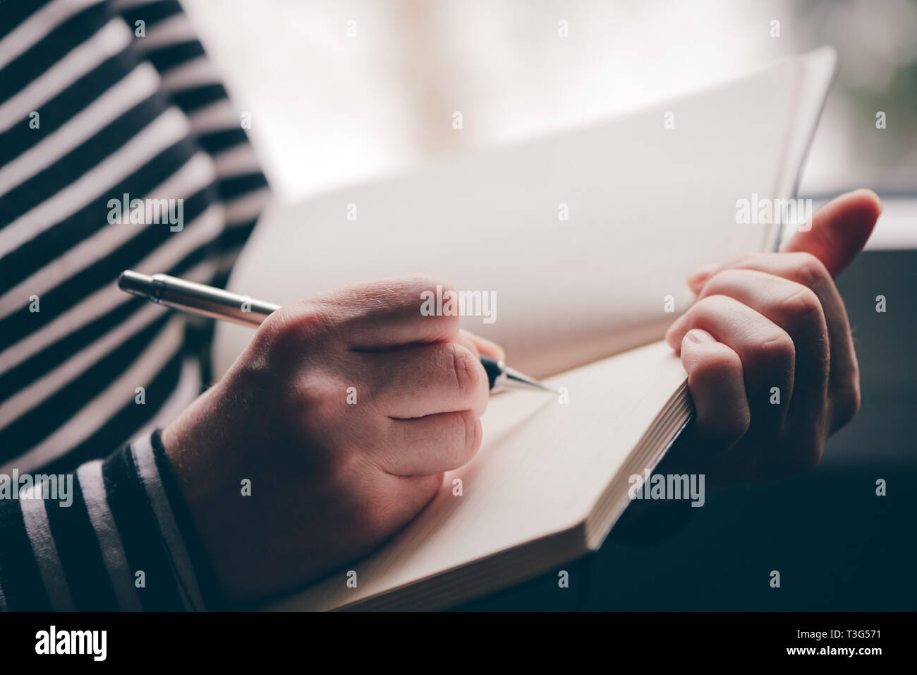 Donna diario di scrittura dalla finestra del suo soggiorno, close up con il fuoco selettivo Foto Stock