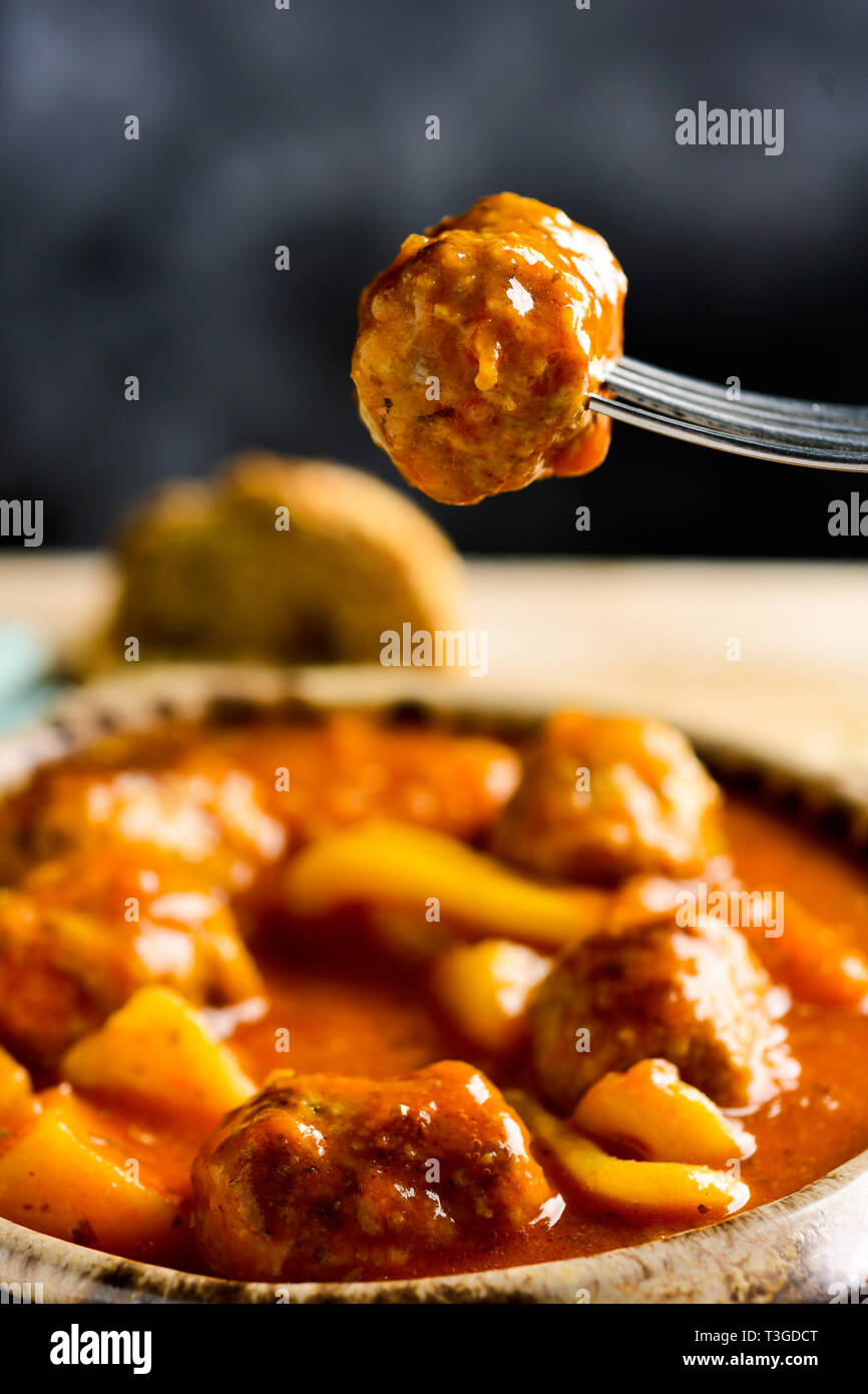 Primo piano di un vaso di terracotta con tipiche albondigas spagnolo con il nero di seppia, polpette con seppie, su una tavola in legno rustico Foto Stock