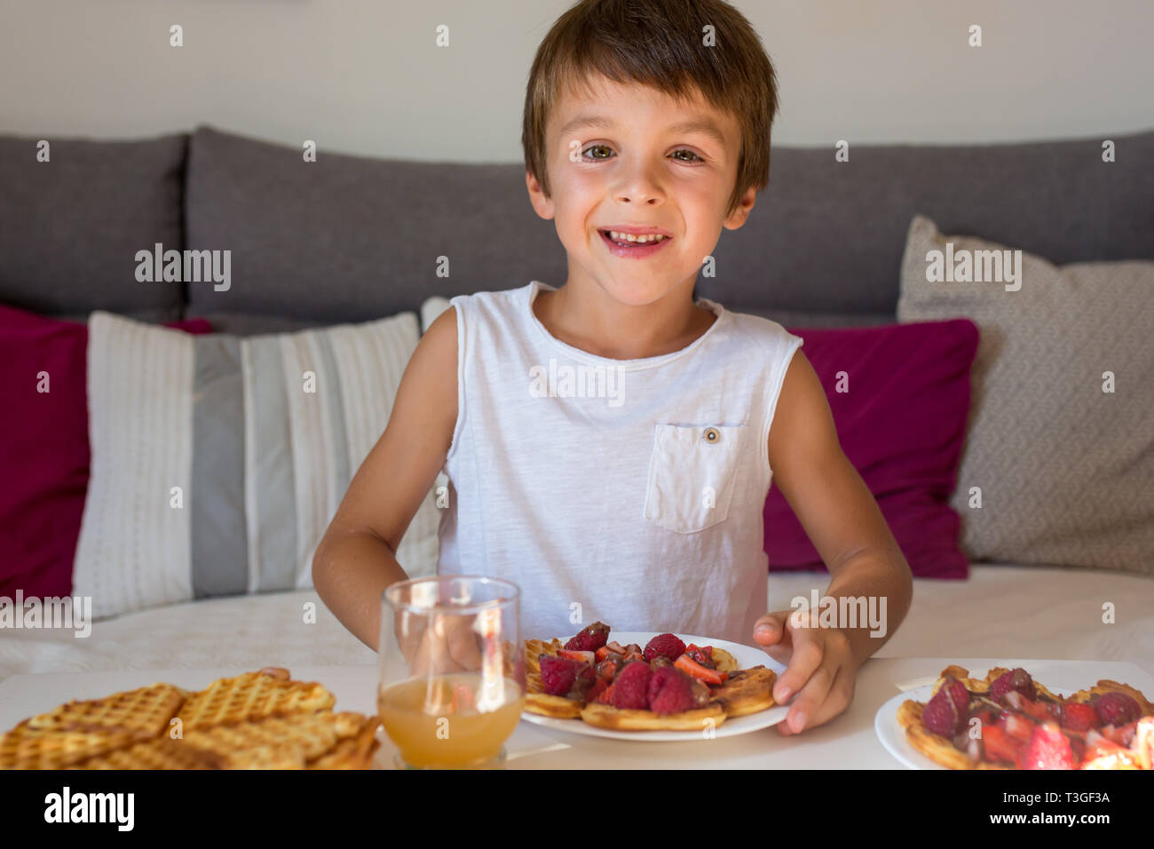 Dolce ragazzo di compleanno, mangiare i waffle belgi con fragole e lamponi e il cioccolato a casa Foto Stock