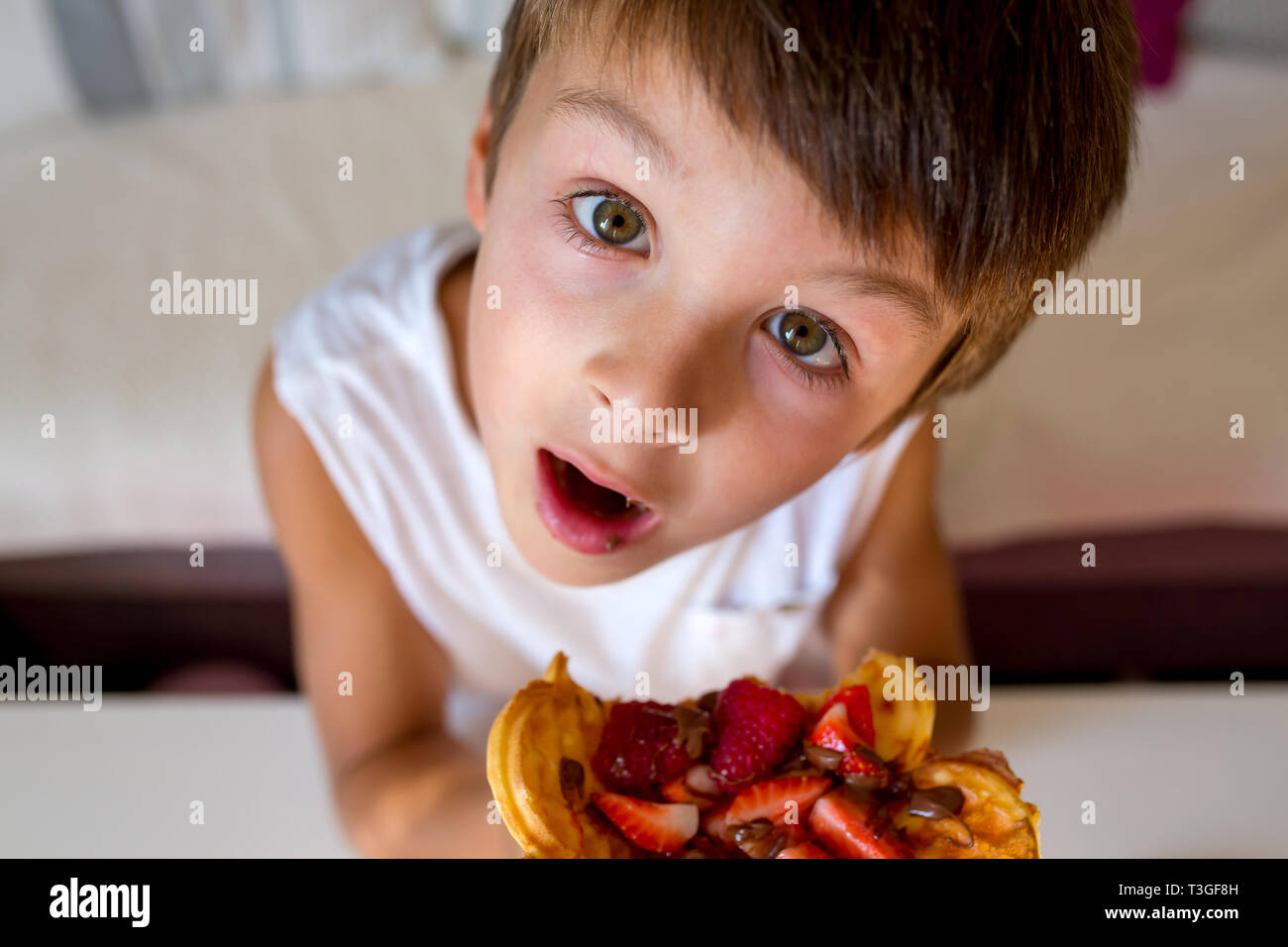 Dolce ragazzo di compleanno, mangiare i waffle belgi con fragole e lamponi e il cioccolato a casa Foto Stock