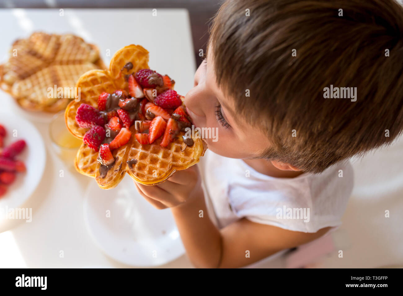 Dolce ragazzo di compleanno, mangiare i waffle belgi con fragole e lamponi e il cioccolato a casa Foto Stock
