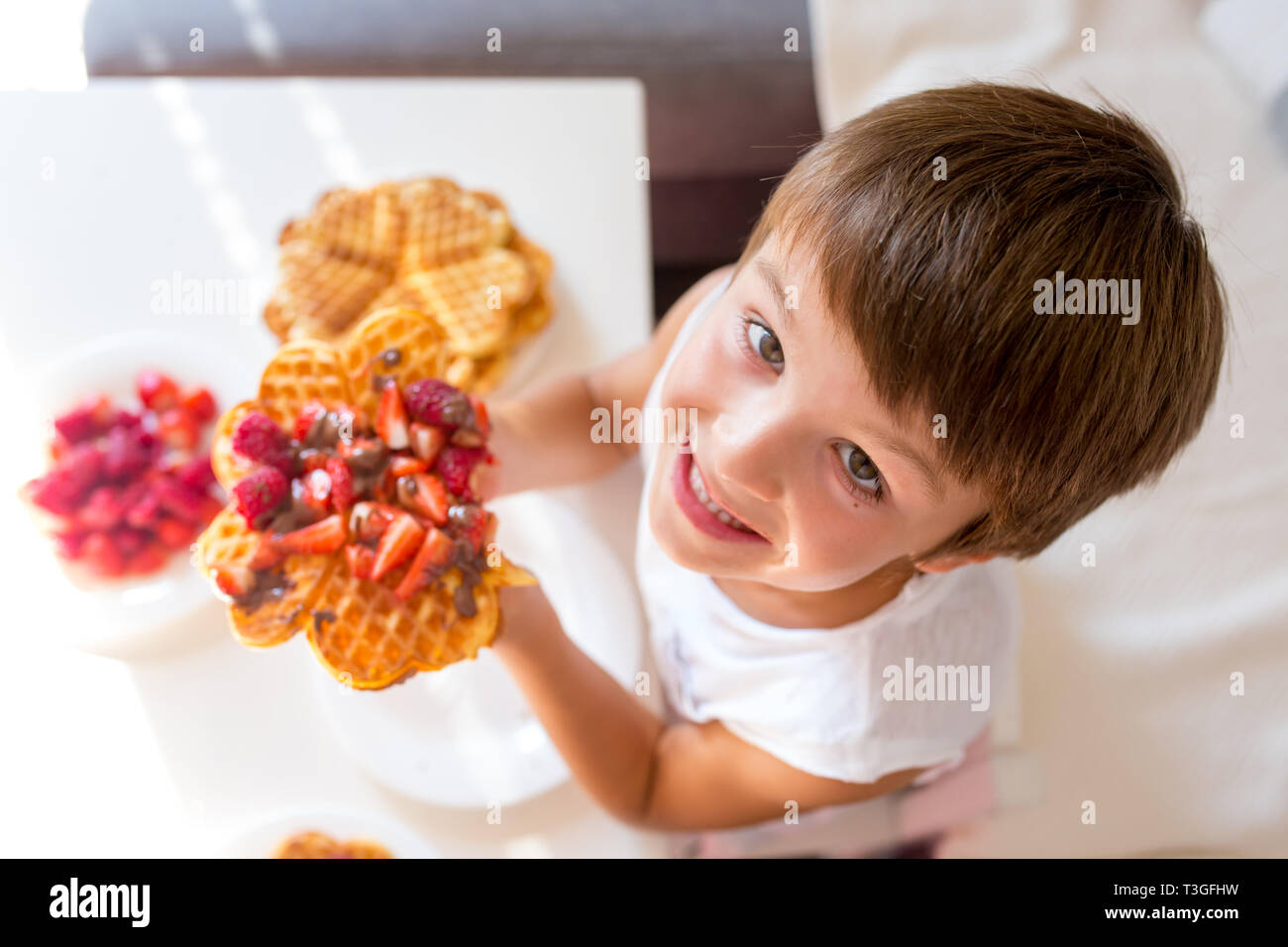 Dolce ragazzo di compleanno, mangiare i waffle belgi con fragole e lamponi e il cioccolato a casa Foto Stock