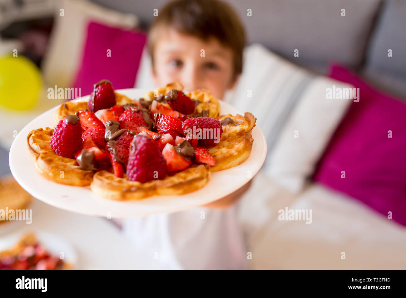 Dolce ragazzo di compleanno, mangiare i waffle belgi con fragole e lamponi e il cioccolato a casa Foto Stock