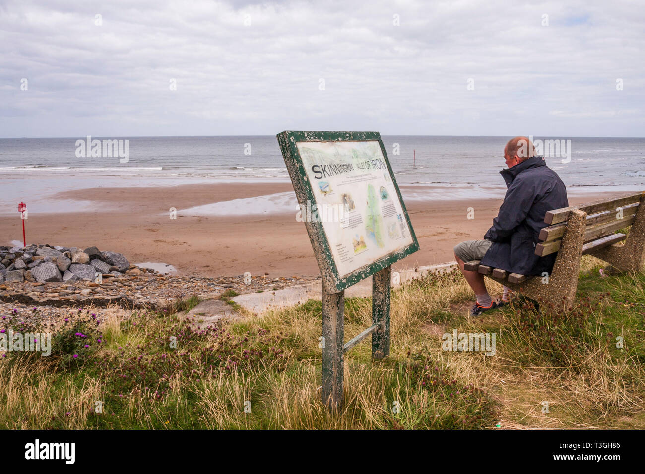 Un uomo maturo seduto su una panchina guardando al mare sulla spiaggia a Skinningrove,North Yorkshire Foto Stock