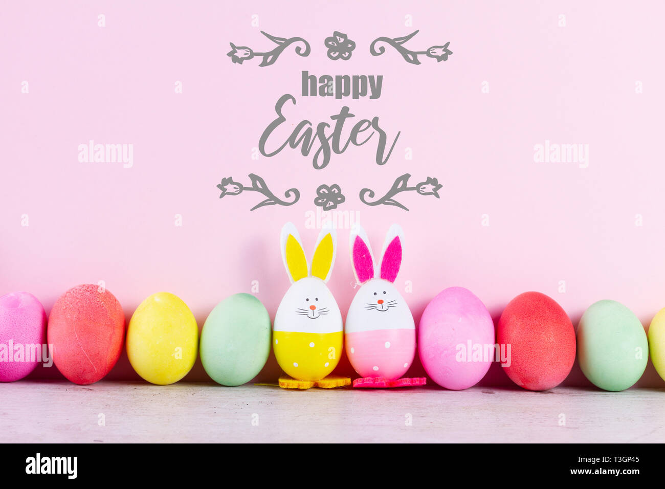 Fila di divertenti conigli pasquali e colorate uova di pasqua sul rosa pastello con sfondo felice Pasqua saluto Foto Stock