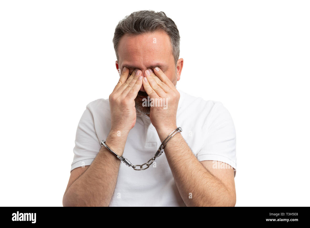 Primo piano dell'uomo che ricopre la faccia con le mani ammanettati come corruzione o ladro concetto isolato su sfondo bianco Foto Stock