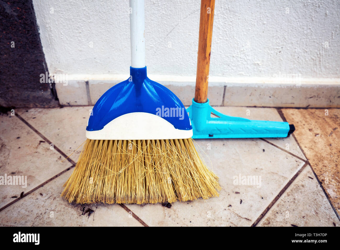 Tergipavimento mop e scopa di spazzamento allineati alla parete e in piedi sul pavimento piastrellato del patio di una casa Foto Stock