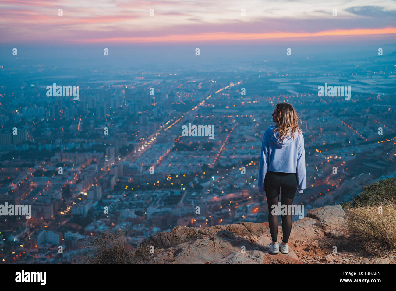 Giovane donna in cima alla montagna in cerca di punti e la città dal di sopra, durante il bel tramonto Foto Stock