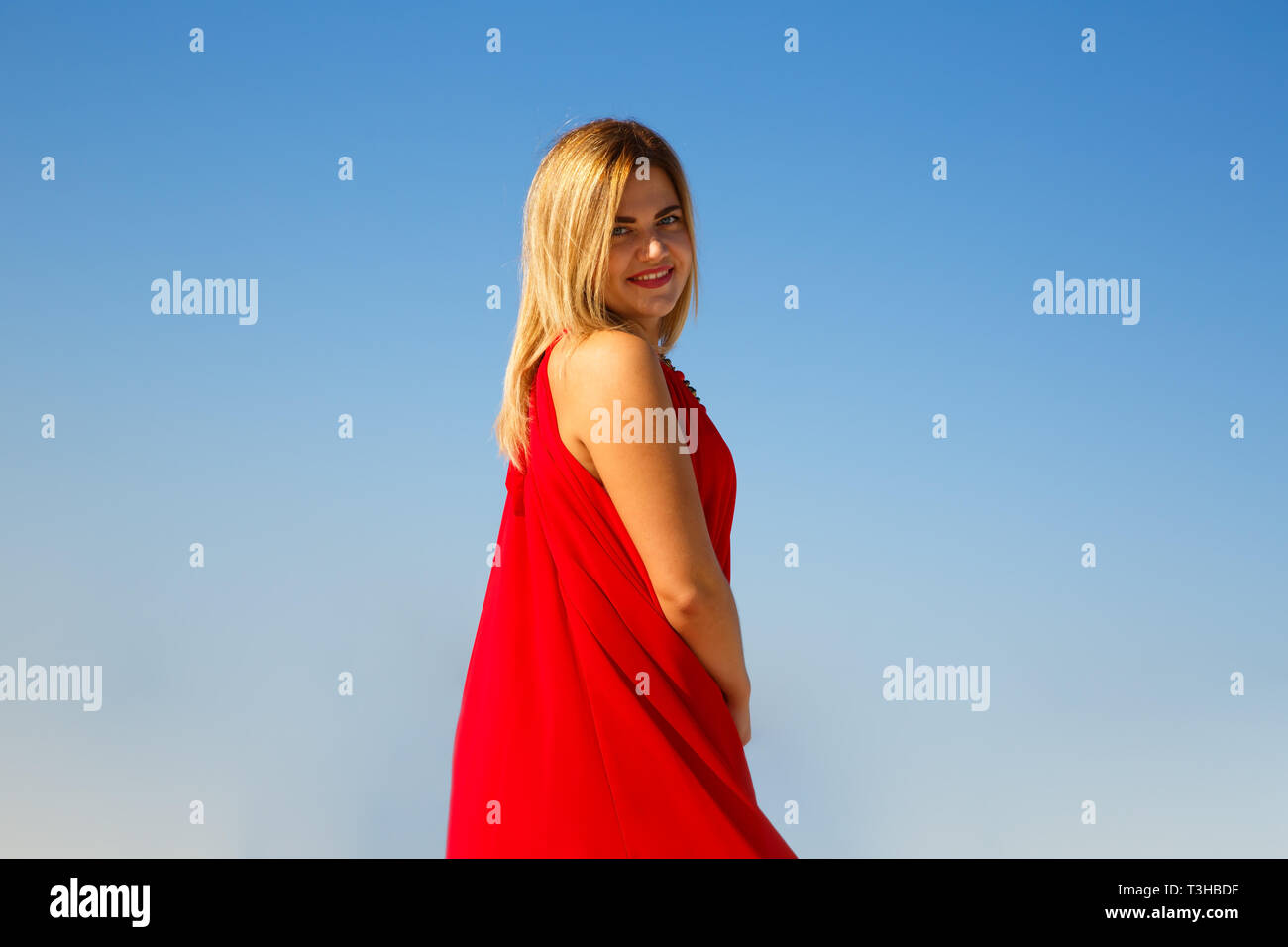 Donna bionda in abito rosso sul cielo blu sullo sfondo. Foto Stock
