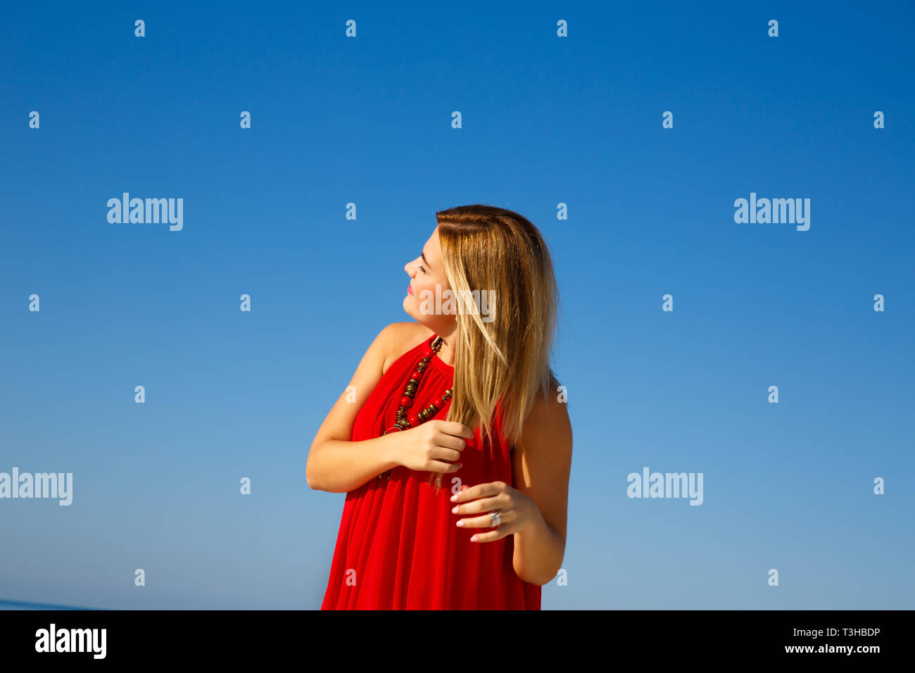 Donna bionda in abito rosso sul cielo blu sullo sfondo. Foto Stock