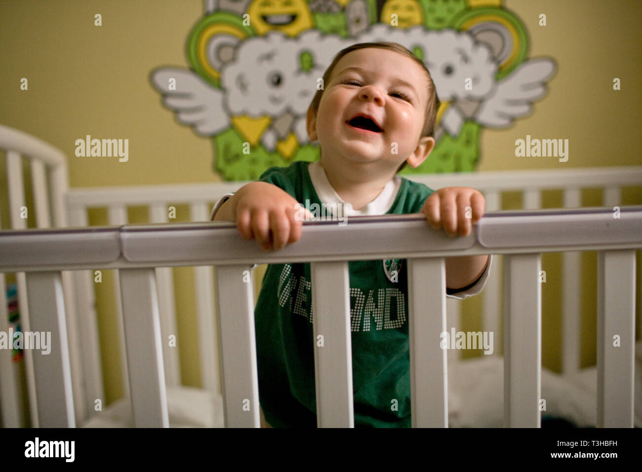 Laughing baby boy in piedi nella sua culla. Foto Stock