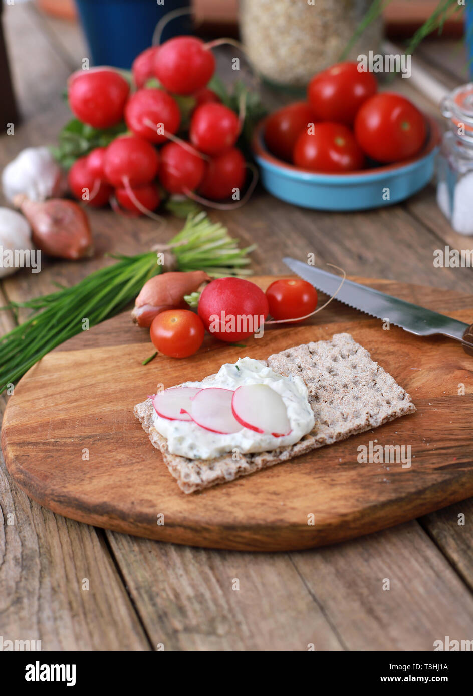 Una sana prima colazione - fette biscottate con quark e di erba cipollina fresca, ravanelli e pomodori su una tavola in legno rustico - una sana colazione con erbe fresche Foto Stock