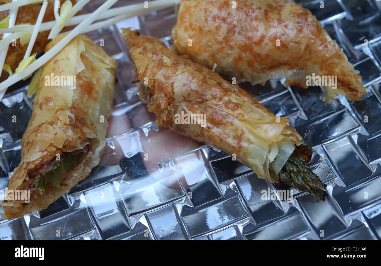 Gli asparagi di rulli rivestiti con i germogli di soia sul piatto di vetro Foto Stock
