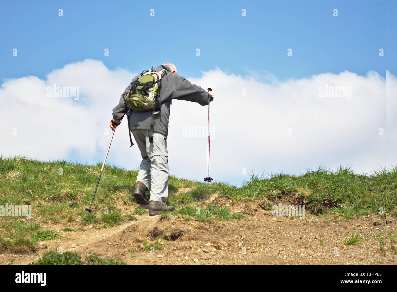 Un anziano gentiluomo mantiene sani e da escursioni fino a un ripido sentiero in un caldo pomeriggio di primavera sulle colline al Parco Olimpico, Monaco di Baviera, Germania Foto Stock