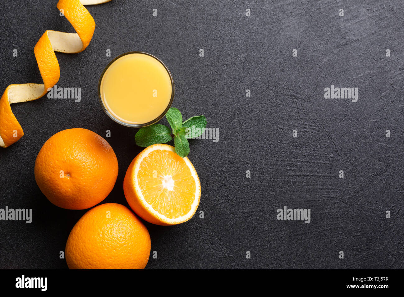 Un gruppo di arance e un bicchiere di succo di frutta su uno sfondo scuro nell'angolo in basso a sinistra del telaio. Vista dall'alto. Foto Stock