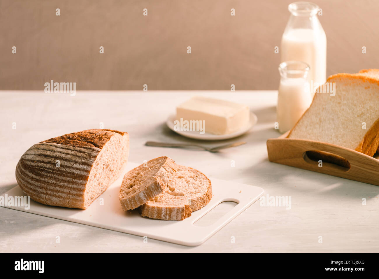 Pane sulla piastra di supporto circondato da burro e latte sul tavolo bianco close-up Foto Stock