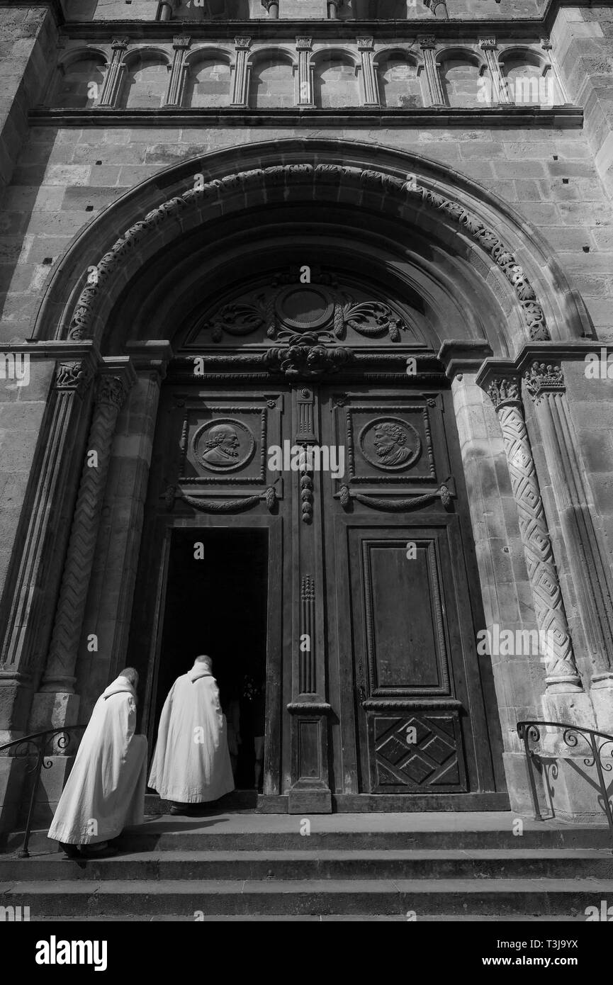 I monaci con il bianco frocks a piedi attraverso il romanico portale di ingresso della cattedrale Saint-Lazare di Autun, Saône-et-Loire, Francia Foto Stock
