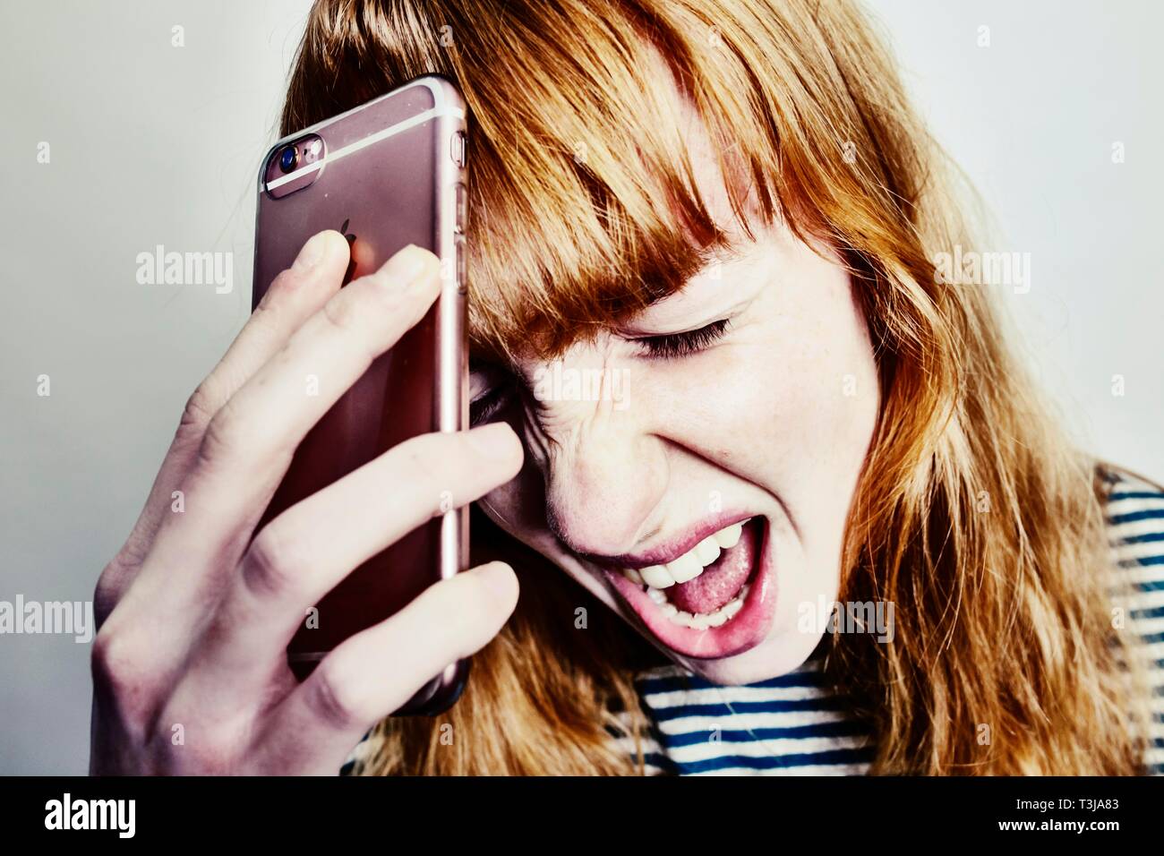 Ragazza adolescente, i capelli rossi, tenendo la testa nella disperazione urlando smartphone, studio shot, Germania Foto Stock