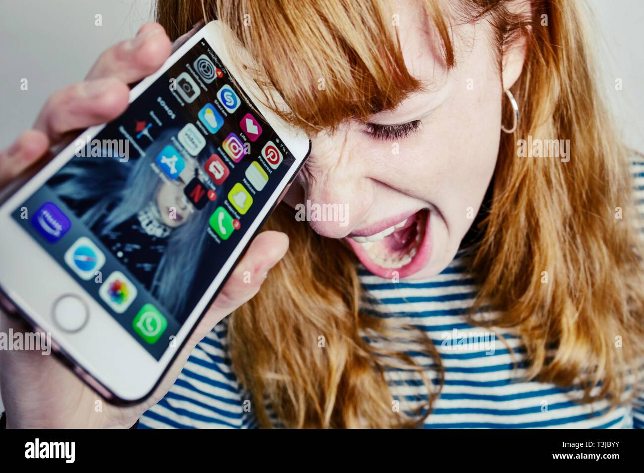 Ragazza adolescente, i capelli rossi, tenendo la testa nella disperazione urlando smartphone, studio shot, Germania Foto Stock